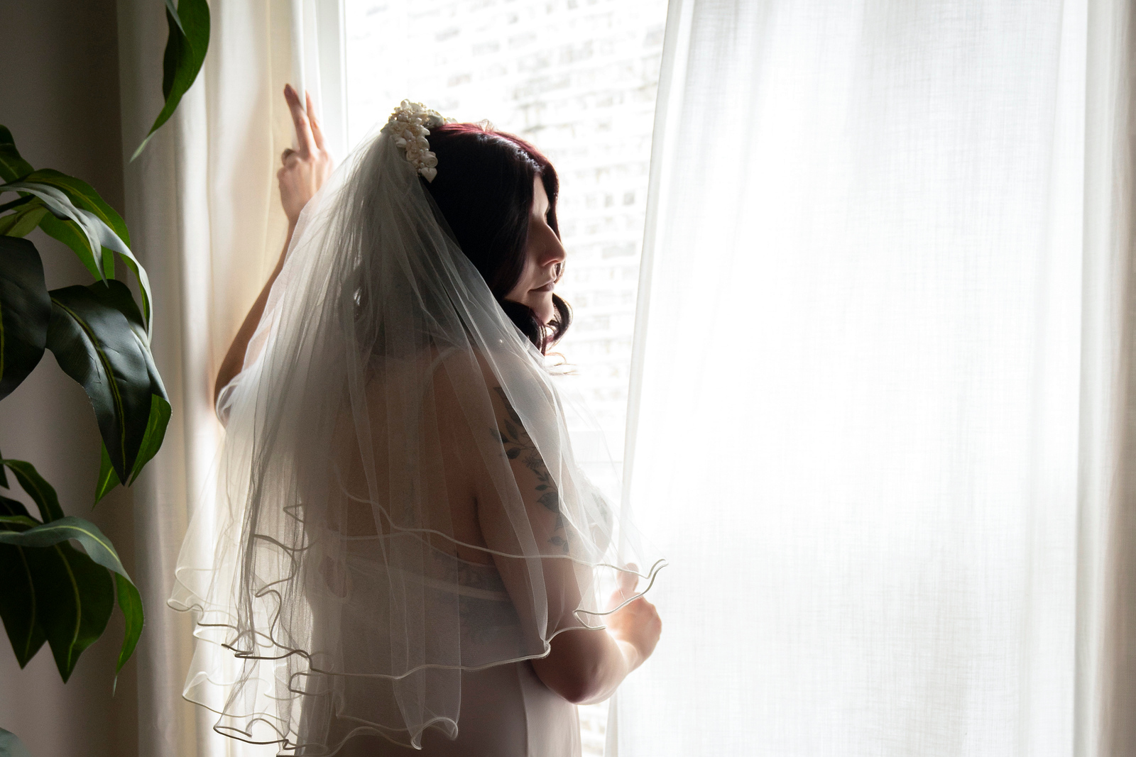 Photograph of a woman standing next to a window with a long veil and lingerie.e