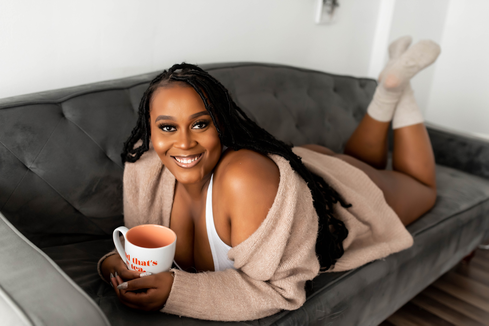 Photo of woman laying down on a couch wrapped in a cozy sweater and holding her coffee